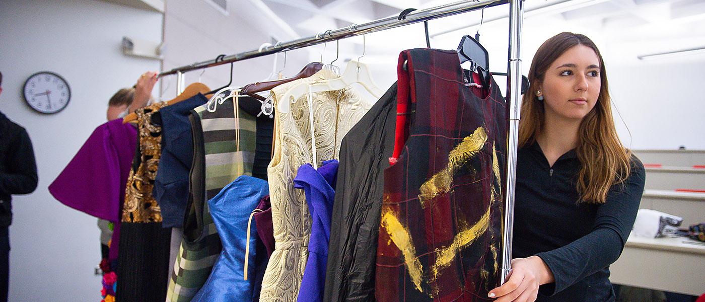 Fashion student moving a rack of designer dresses through the dressing area