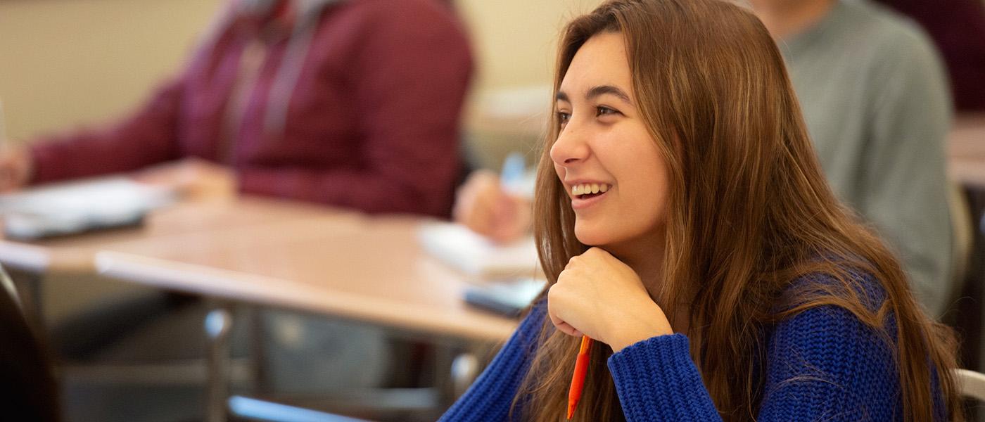 数学女学生坐在她的课桌上，在课堂上微笑.