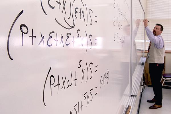 Mathematics professor working on equations on whiteboard